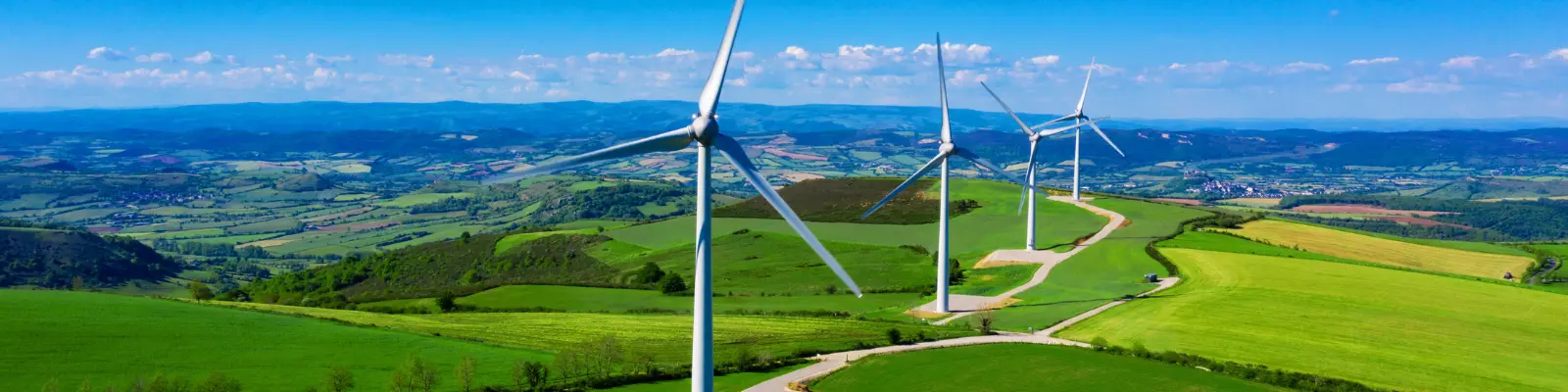 A wind farm in a field with a blue sky and clouds